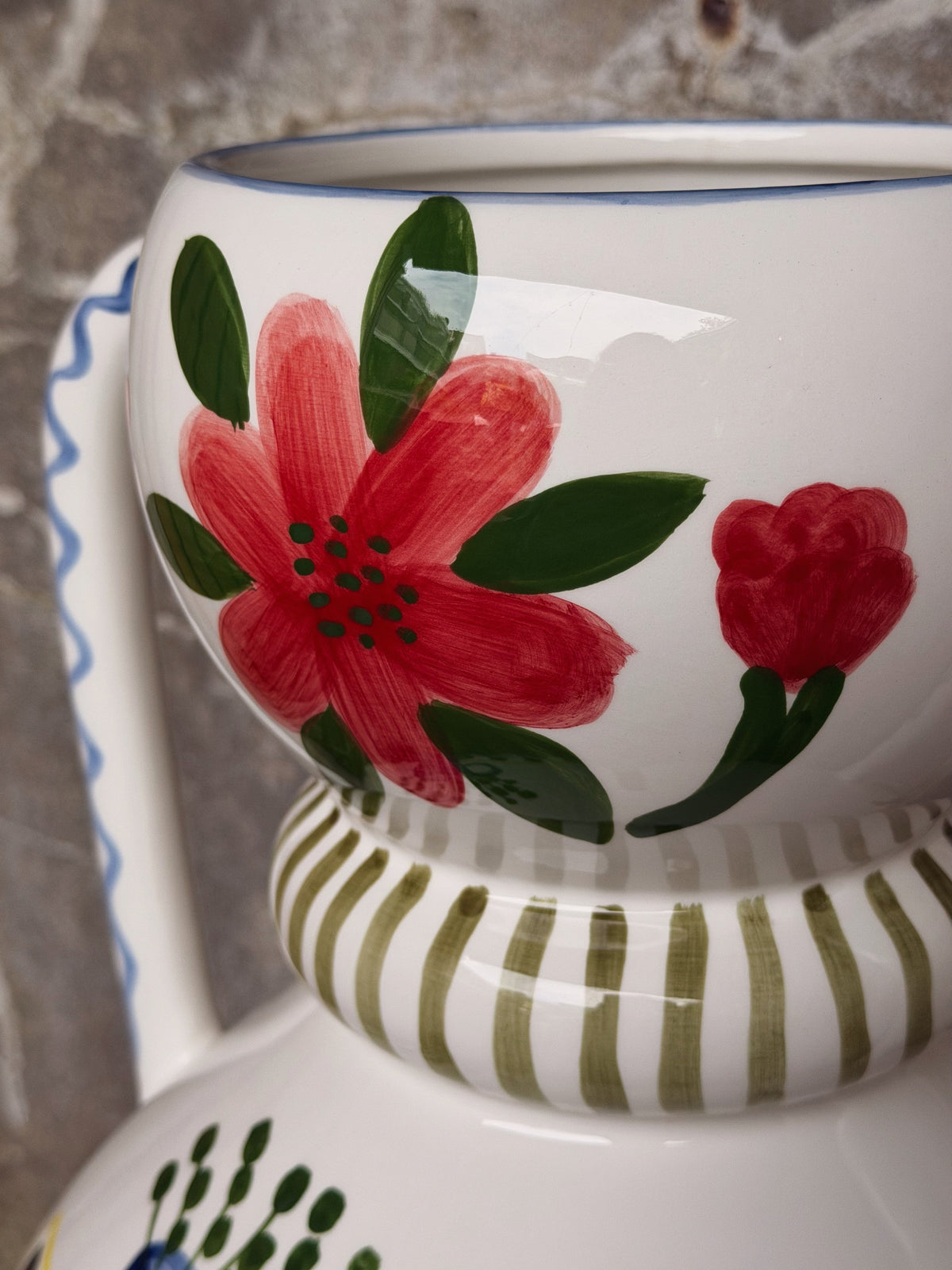 Detail van de handgeschilderde rode bloem met groene blaadjes boven de gestreepte band