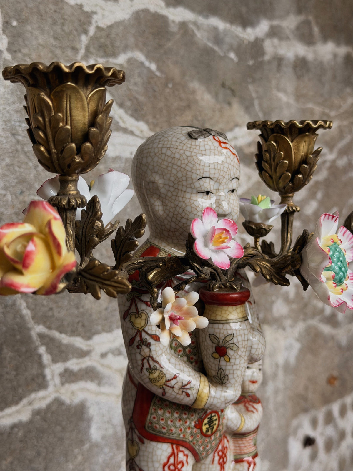 Close-up van de twee bronzen kaarshouders met porseleinen roos en bloesems boven het kindfiguur