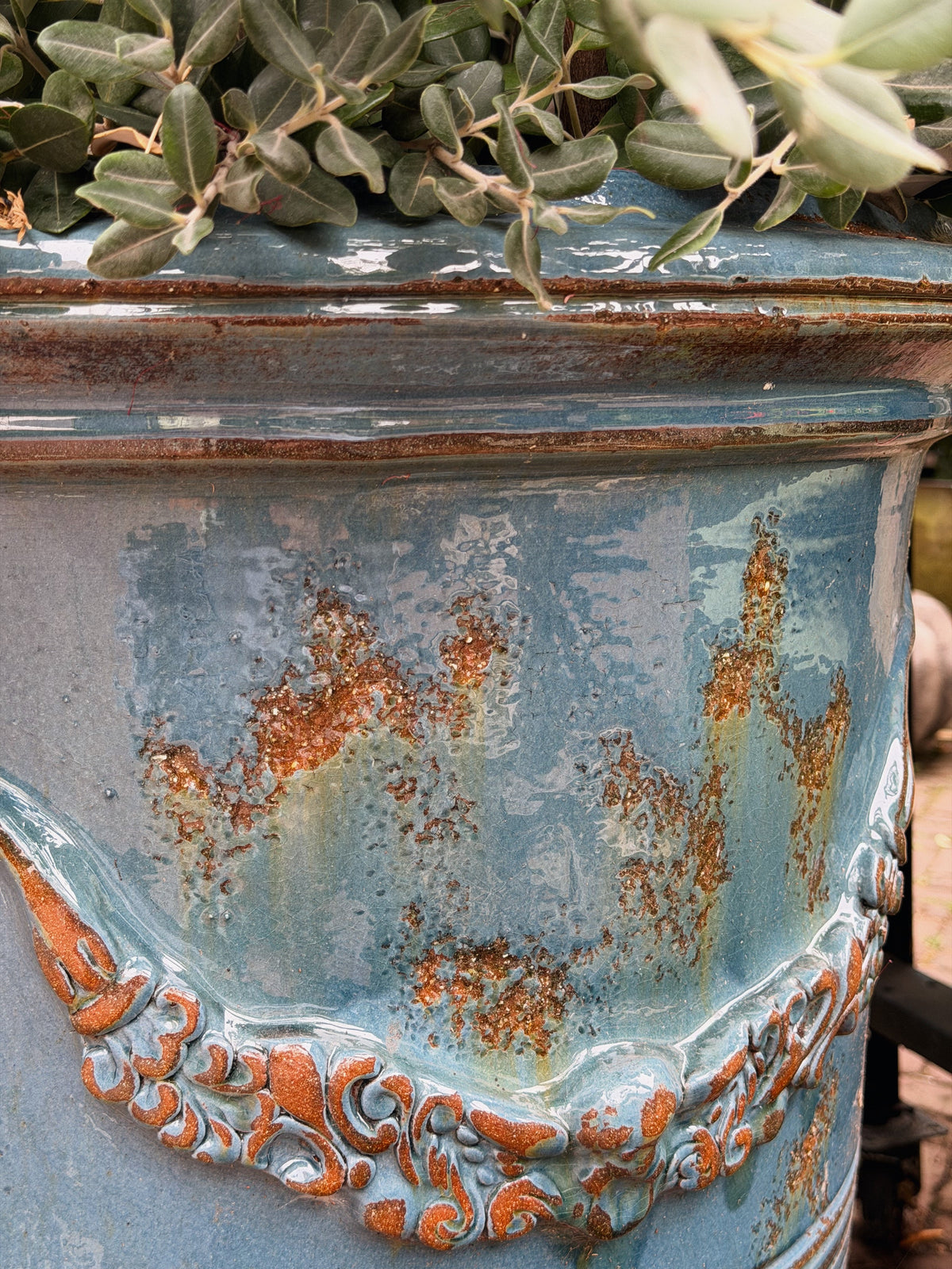 Close-up van de blauwgroene glazuurlaag met roestbruine vlekken en het bloemguirlande-reliëf