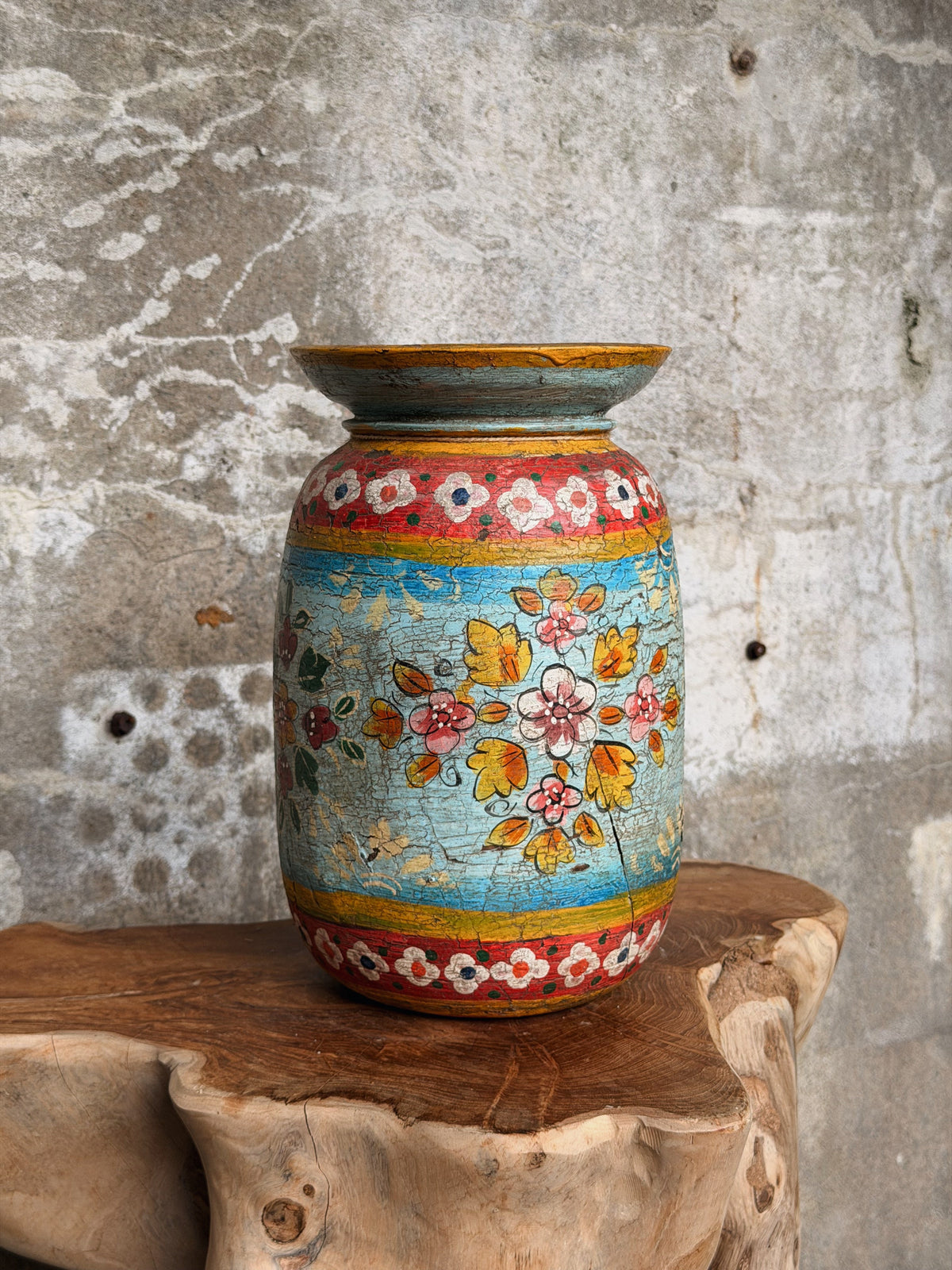 Melkpot op een boomstamtafel, gele en roze bloemen op turquoise met rode bloemenbanden