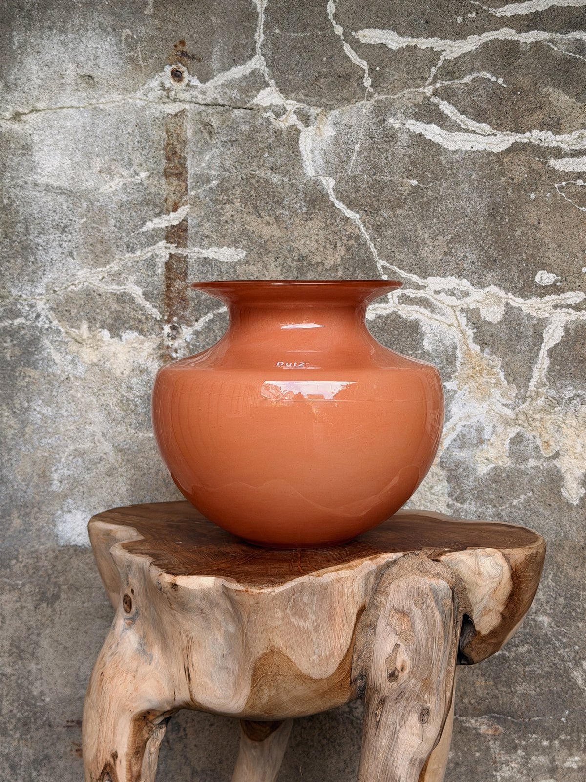 Bolle terracotta-oranje vaas met uitlopende rand op een houten boomstamkruk
