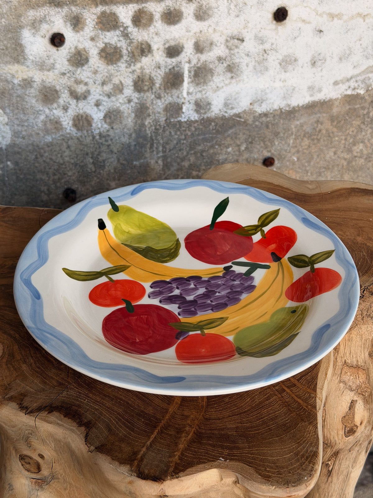 Het fruitbord schuin van opzij, met golvende blauwe rand, gele bananen en paarse druiven
