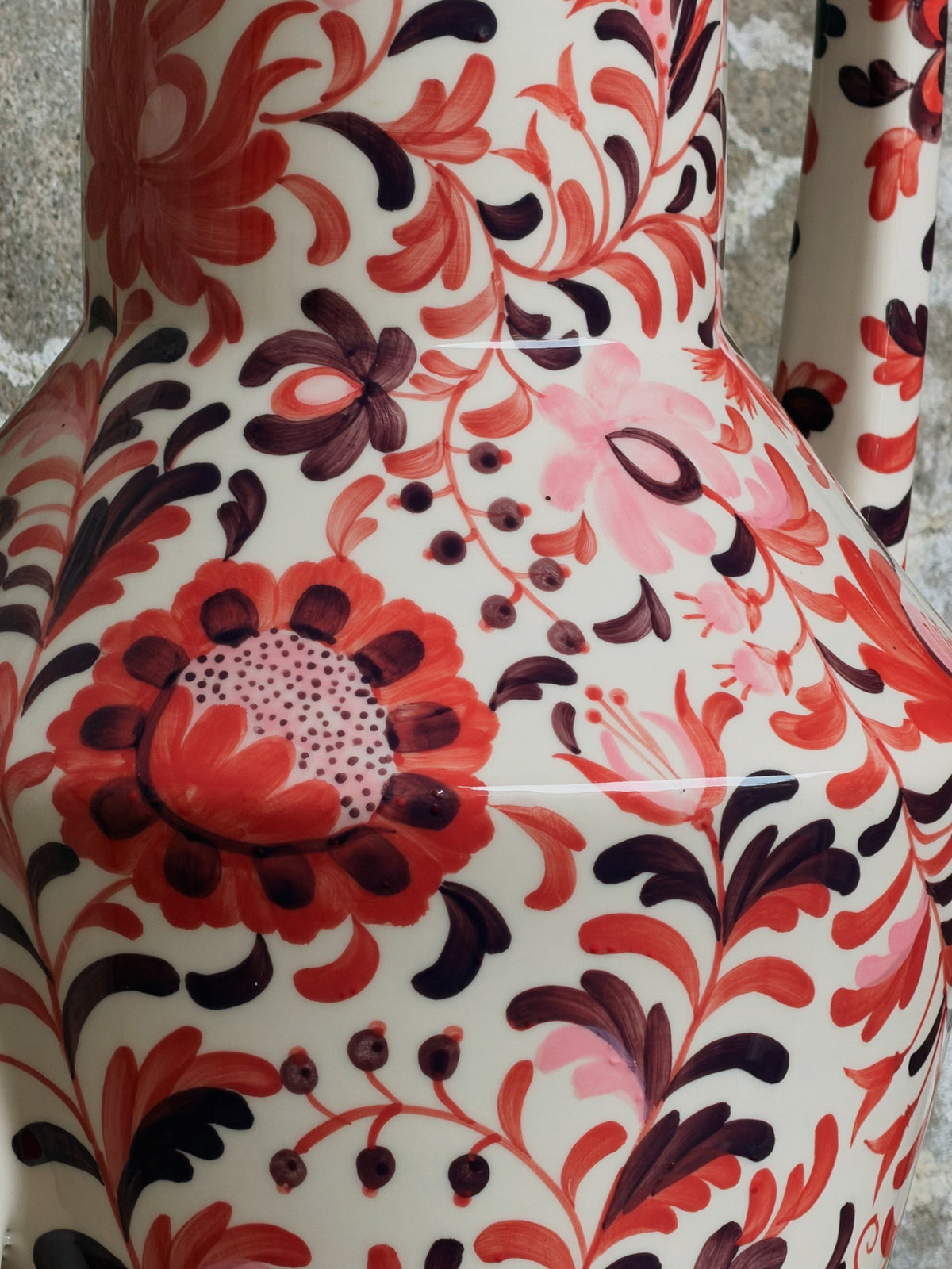 Close-up van het handgeschilderde bloemmotief in rood, roze en donkerpaars op crème glazuur