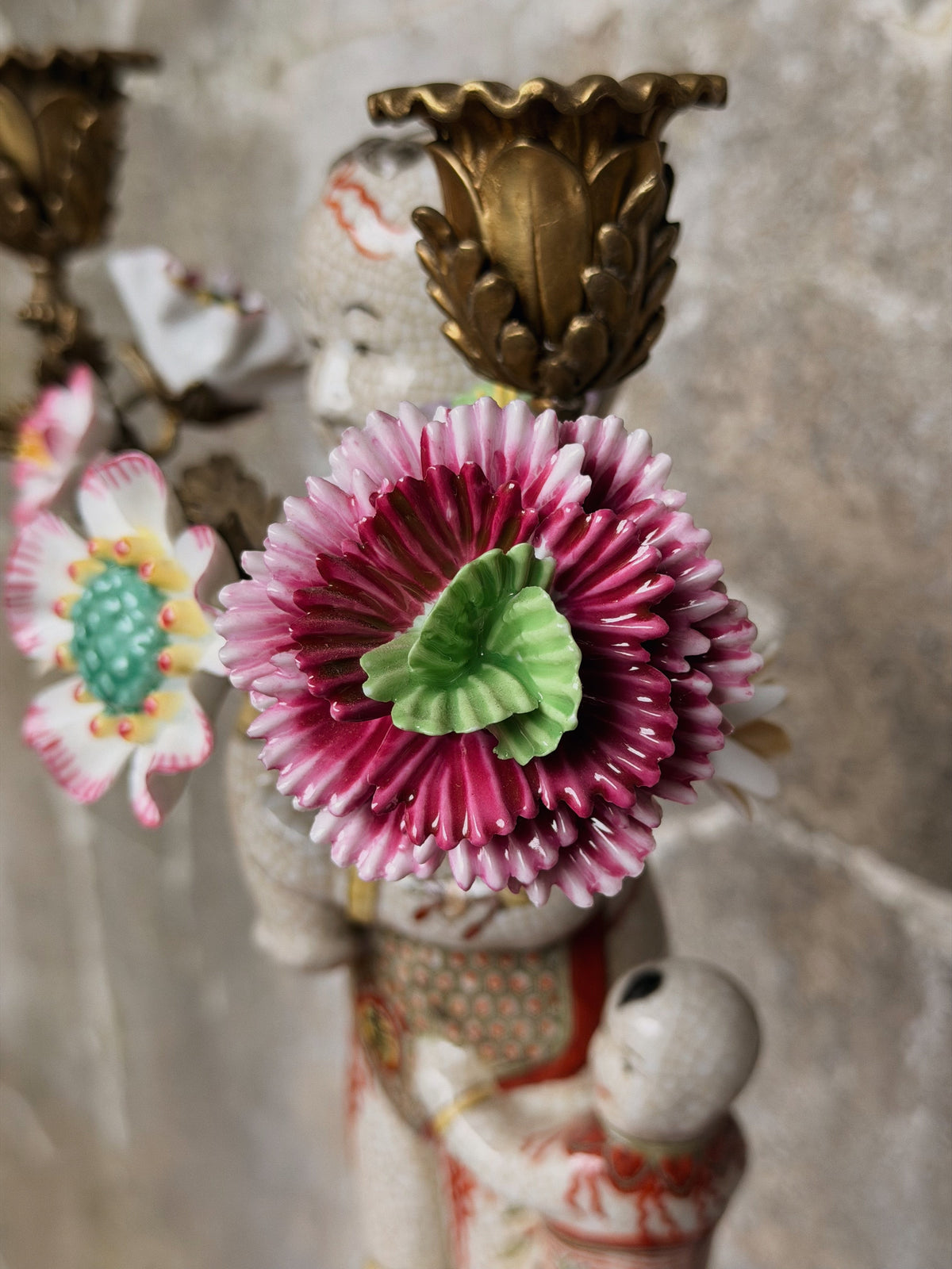 Detail van een gelaagde roze-paarse porseleinen bloem met groen hart naast een bronzen kaarshouder