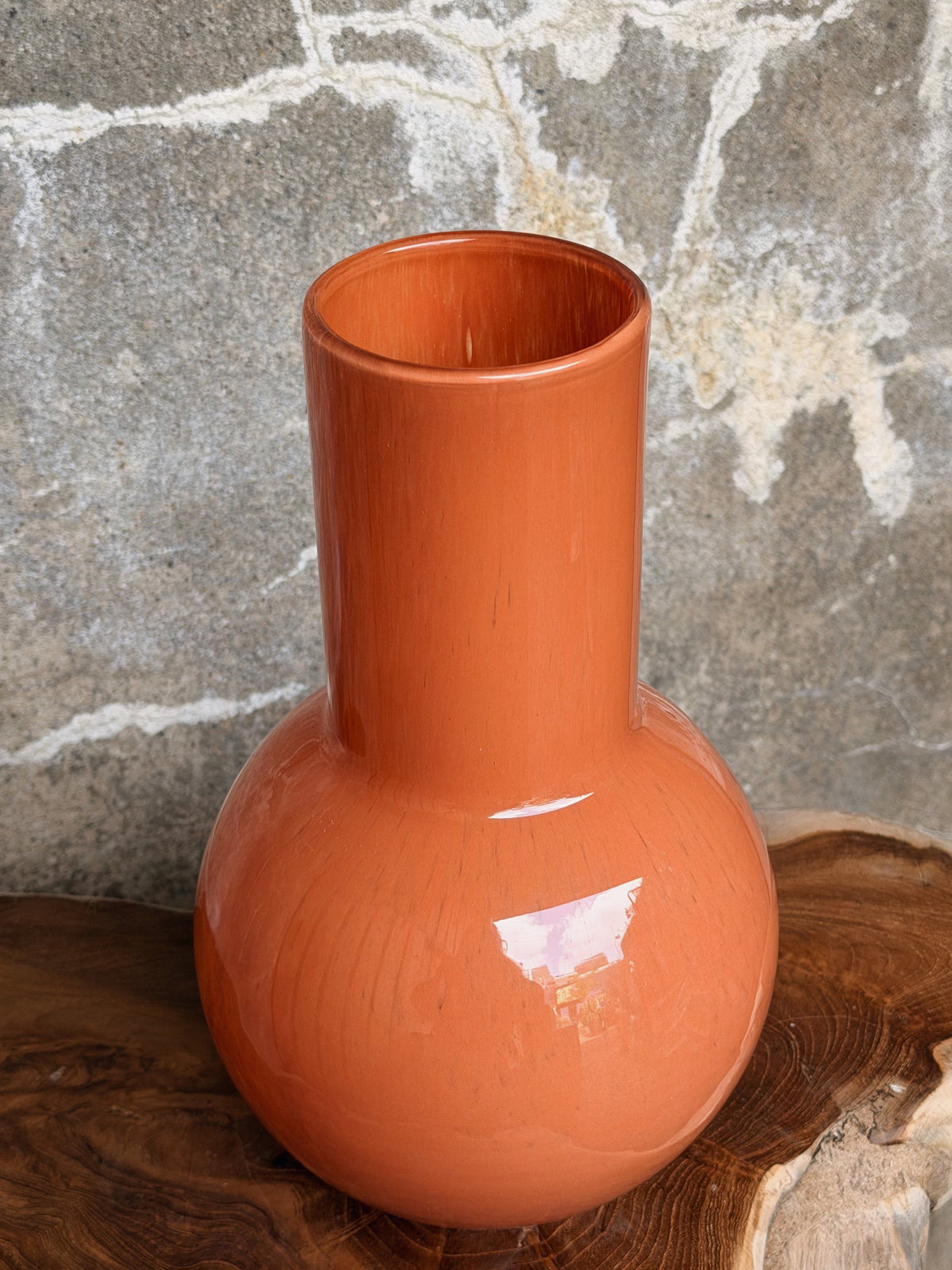 Close-up van de open hals en glanzende bolling van de oranje vaas, van bovenaf gezien