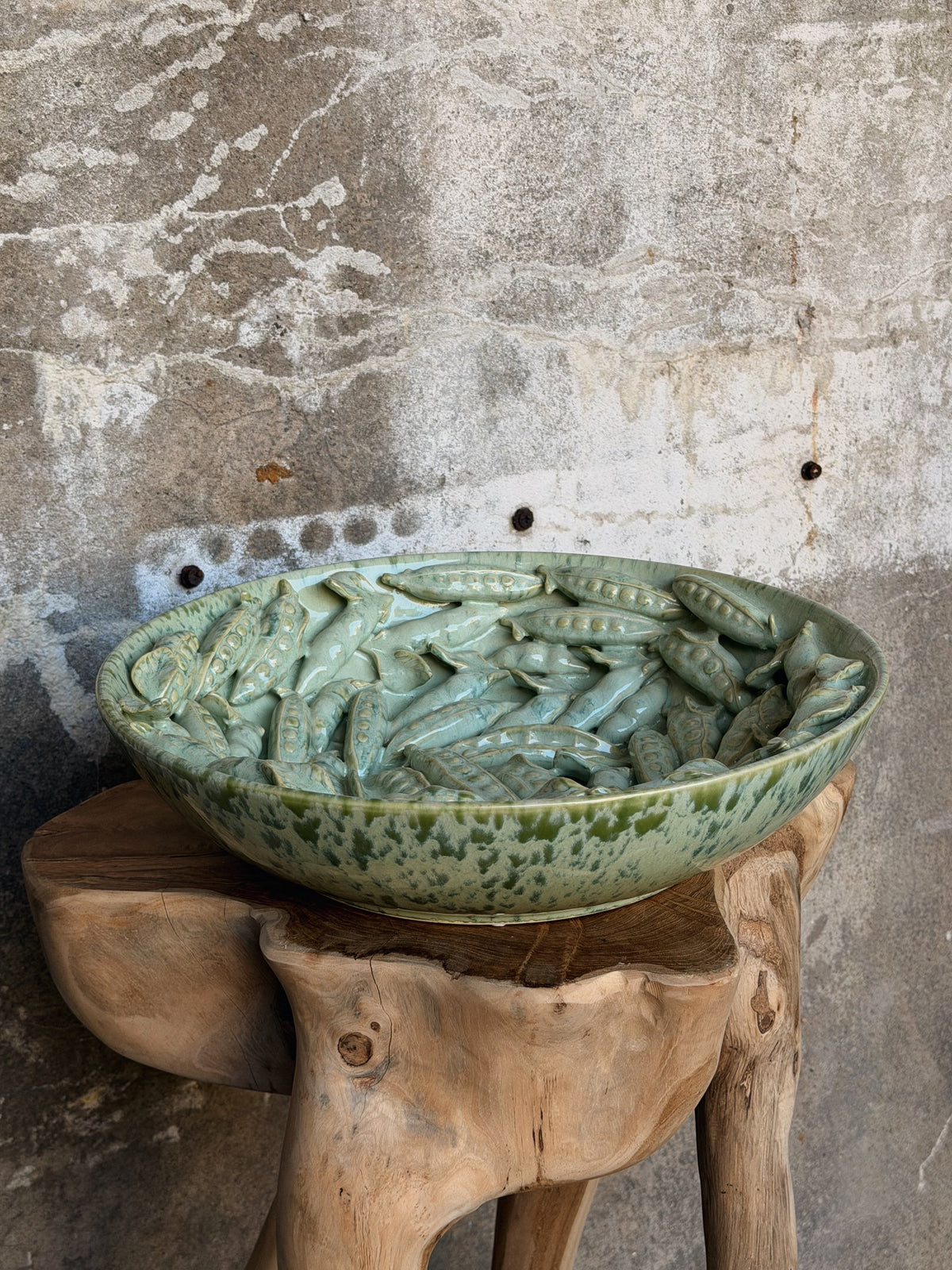 Groene keramische schaal vol reliëf van erwtenpeulen, op een houten kruk tegen een betonnen muur