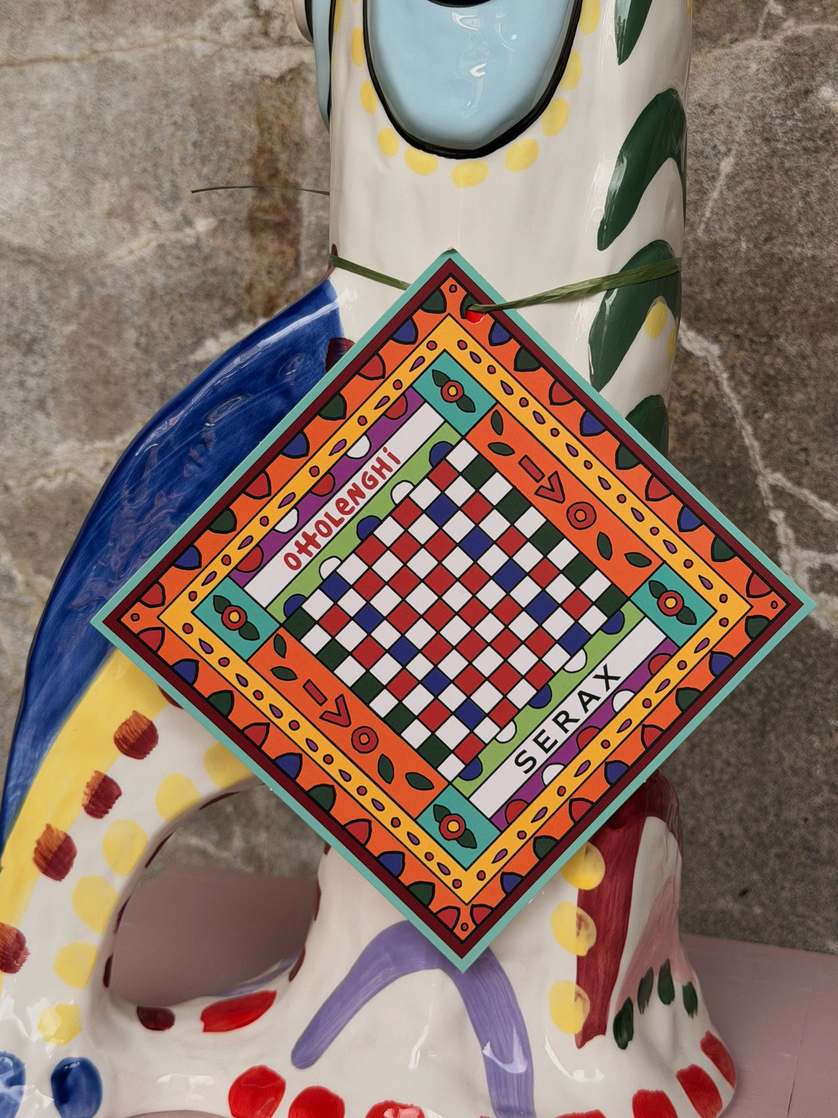 Ruitvormig Ottolenghi-Serax label met kleurige tegelprint, hangend aan de beschilderde vaas