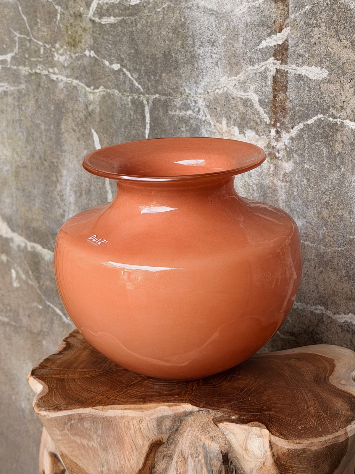 Zijaanzicht van de bolle oranje vaas met wijd uitlopende rand op een ruw houten blad