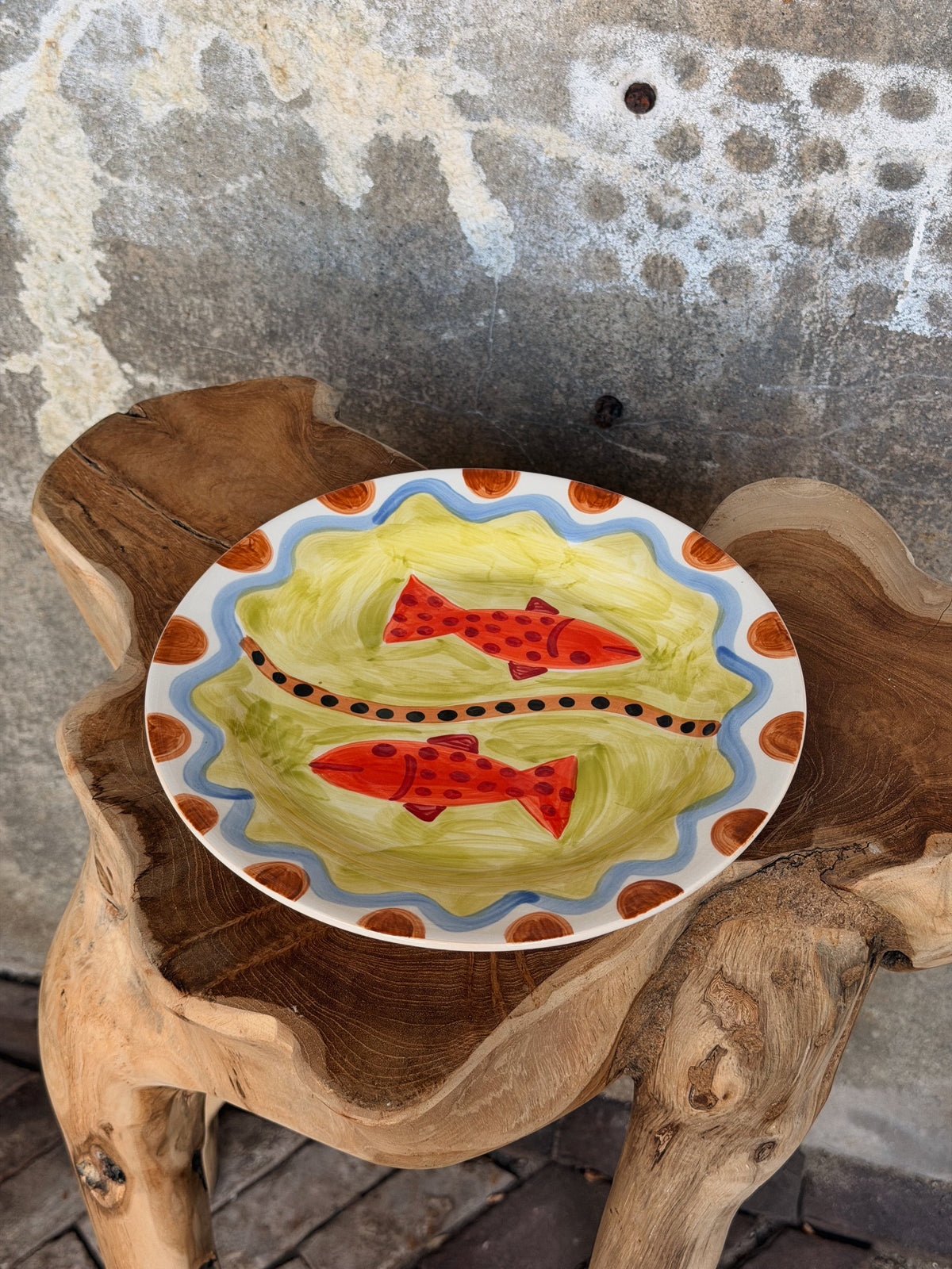 Bord met twee rode gestippelde vissen op groen, met blauwe golfrand en terracotta stippen