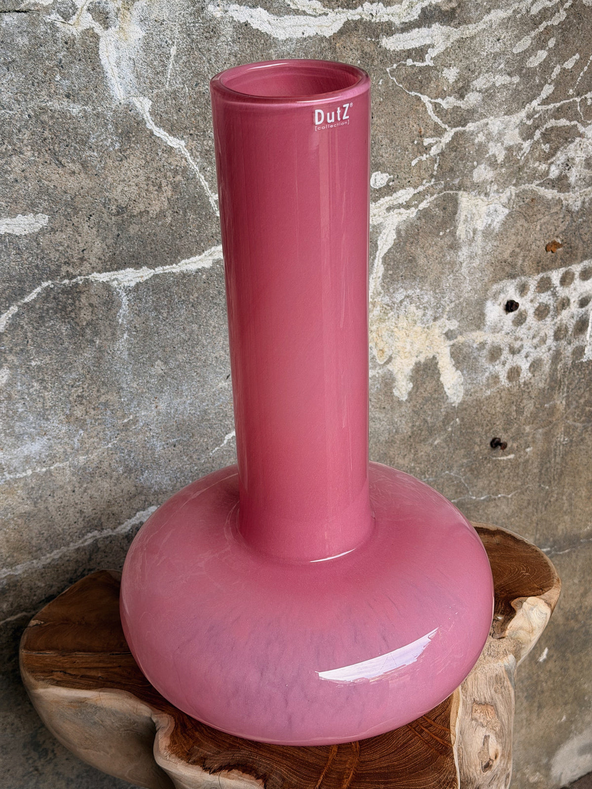 Roze vaas met hoge cilinderhals van dichtbij, met zicht in de ronde opening, tegen een betonnen muur