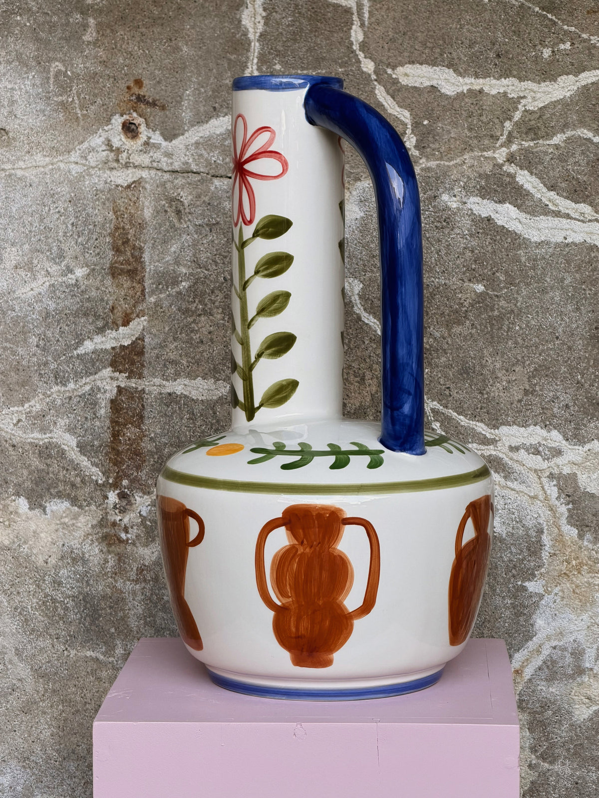 Handbeschilderde kruikvaas met blauw oor en oranje amforen, frontaal op de lichtroze sokkel