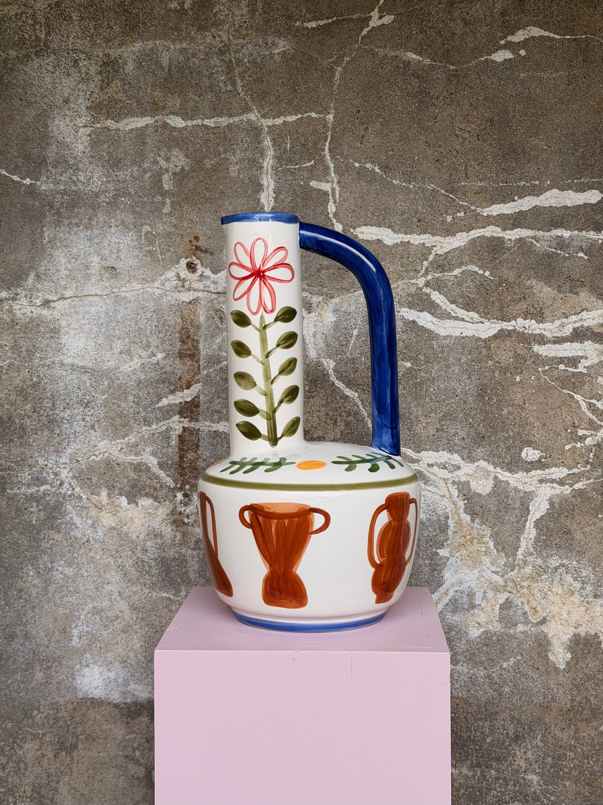 Witte kruikvaas met blauw oor, rode bloem op de hoge hals en oranje amforen, op een roze sokkel