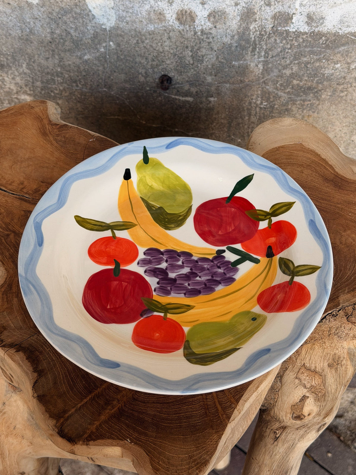 Wit bord met blauwe golfrand en geschilderd fruit: bananen, appels, peren en een druiventros