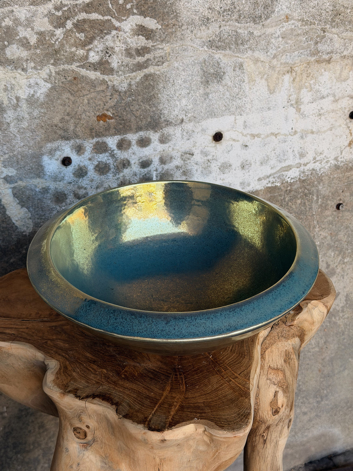 Ronde schaal met blauwgroen glazuur en gouden gloed, bovenaanzicht op een houten kruk
