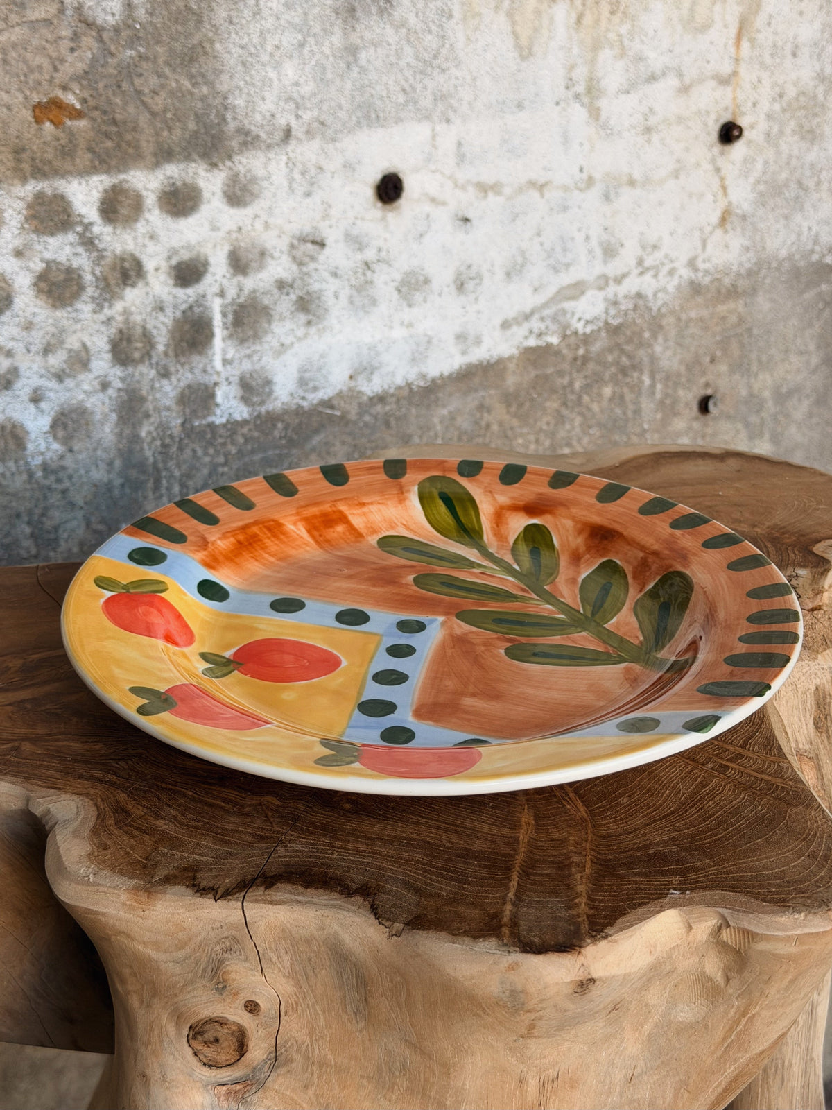 Schuin aanzicht van het oker-terracotta bord met olijftak, tomaten en gestippelde rand